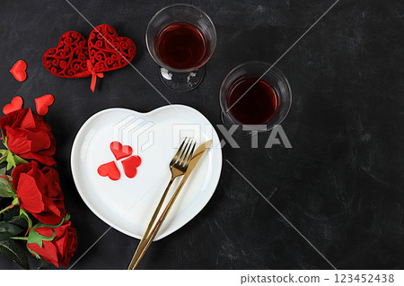 Festive table setting, menu design for Valentine's Day, cutlery with a heart on a plate and glasses with red wine, festive composition with a bouquet of red roses, kitchen background. Selective focus 123452438