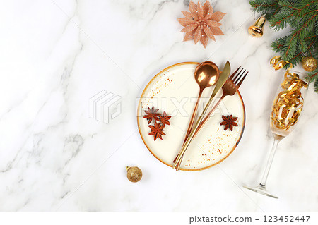 Christmas table setting. Festive New Year's cutlery with a napkin on a plate on a marble concrete background, festive composition with fir branches and a glass of champagne, kitchen background. Christmas table setting. Festive New Year's cutlery with a napkin on a plate on a marble concrete background, festive composition with fir branches and a glass of champagne, kitchen background. 123452447