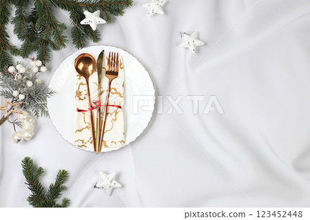 Christmas table setting. Festive New Year's cutlery with a napkin on a plate on a marble concrete background, festive composition with fir branches and a glass of champagne, kitchen background. 123452448