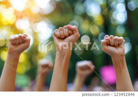 Participants in a peaceful protest raise their fists in solidarity showcasing determination and unity. The setting is a lush park filled with trees during early afternoon light. 123452846
