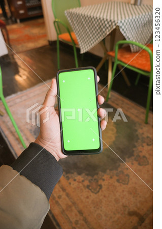 Hand holding a smartphone with a blank green screen in a cafe 123456320