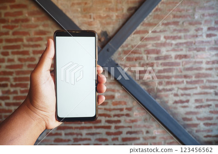 Hand holding a smartphone against a rustic brick wall backdrop 123456562