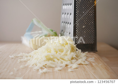Shredded cheese beside a grater on a wooden kitchen counter Shredded cheese beside a grater on a wooden kitchen counter 123456707