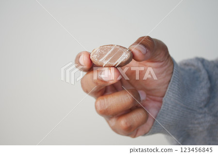 Hand holding a small, oval-shaped candy with stripes indoors Hand holding a small, oval-shaped candy with stripes indoors 123456845