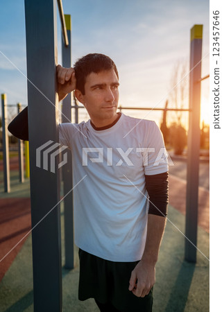 young athletic man resting after fitness calisthenics workout at street gym during sunset, taking a break during body improvement and strength training young athletic man resting after fitness calisthenics workout at street gym during sunset, taking a break during body improvement and strength training 123457646
