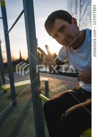 cheerful athletic man resting after exercising abs bench crunch at fitness calisthenics workout at street gym during sunset, relax after body improvement and strength training concept 123457665