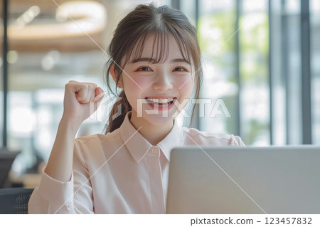 年輕女子在筆記型電腦前工作時,微笑著雙手高興地握緊 年輕女子在筆記型電腦前工作時,微笑著雙手高興地握緊 123457832