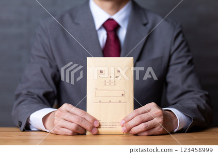 A middle-aged male businessman wearing a gray suit and holding a pay envelope A middle-aged male businessman wearing a gray suit and holding a pay envelope 123458999