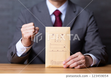 A middle-aged male businessman wearing a gray suit and holding a pay envelope and making a fist pump 123459054