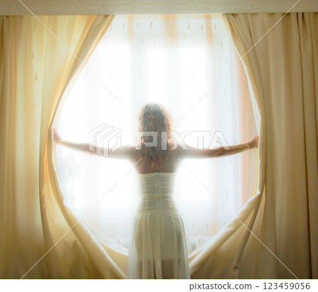 girl opening curtains in a bedroom 123459056