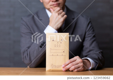 一位身穿灰色西裝、手持薪水信封的中年男性商人擔心 123459082