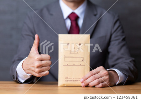 一位身穿灰色西裝、手拿薪資袋、豎起大拇指的中年男性商人 123459361