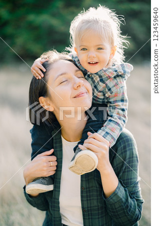 Happy little girl hugging her mom head while sitting on her shoulders. Portrait Happy little girl hugging her mom head while sitting on her shoulders. Portrait 123459640