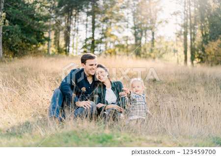 Little girl sits on the lawn next to hugging mom and dad 123459700