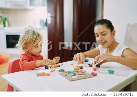 Mom with a little girl make crafts from plasticine at the table 123459712