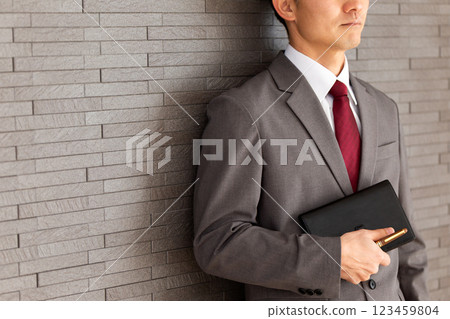 A middle-aged male businessman in a gray suit leaning against a wall 123459804
