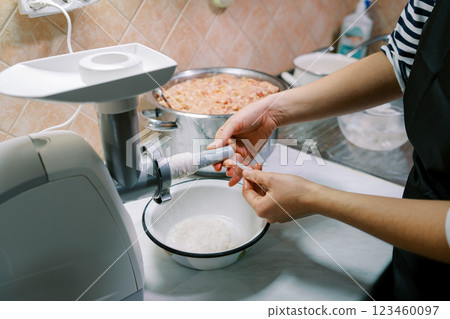 Housewife puts an intestine on a sausage attachment on an electric meat grinder Housewife puts an intestine on a sausage attachment on an electric meat grinder 123460097