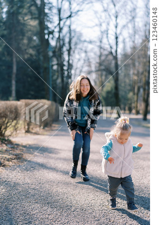 Smiling mother leaned forward watching little girl walking down the road 123460148