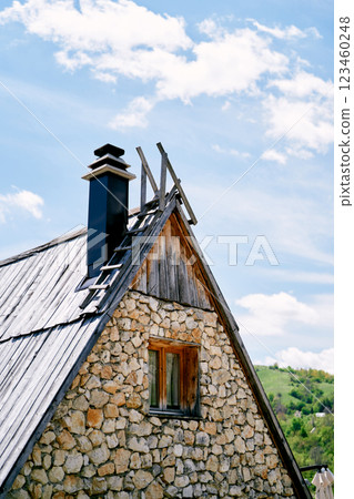 Triangular roof of a stone house with stairs and chimney against a cloudy sky 123460248