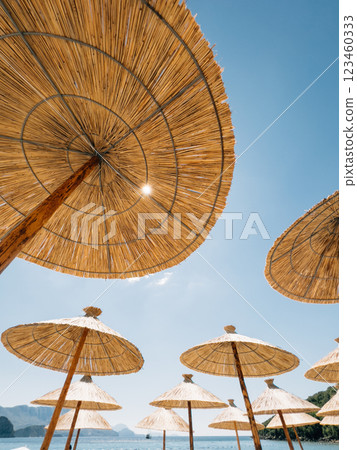 Straw sun umbrellas on the beach by the sea against the blue sky 123460333