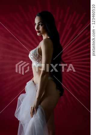 Elegant bride in lingerie poses gracefully against a red backdrop 123460510