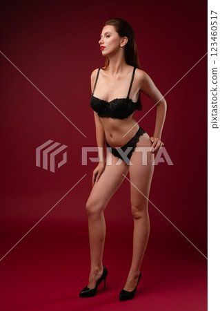 Confident woman poses in elegant lingerie against a bold red background Confident woman poses in elegant lingerie against a bold red background 123460517
