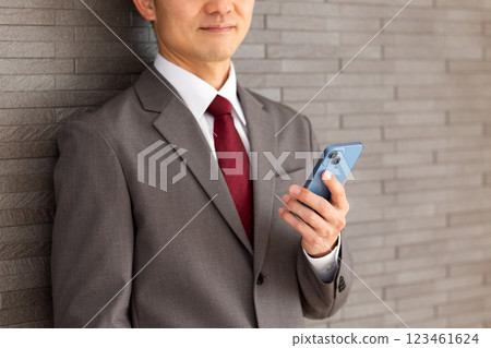 身穿灰色西裝、手持智慧型手機的中年男性商人 身穿灰色西裝、手持智慧型手機的中年男性商人 123461624