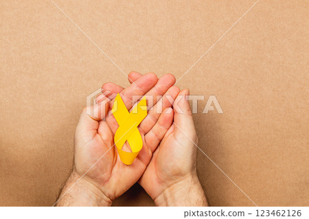 Hands holding a yellow ribbon symbolizing cancer awareness and hope Hands holding a yellow ribbon symbolizing cancer awareness and hope 123462126