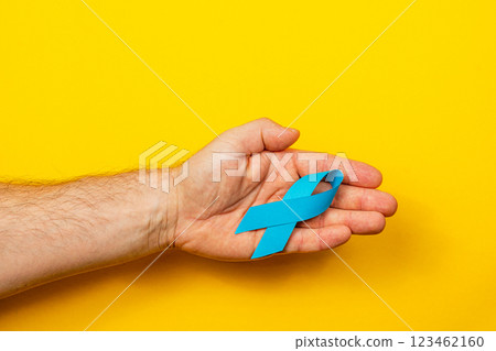 Hand holding a blue ribbon symbolizing cancer awareness and support 123462160