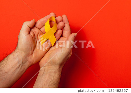 Hands holding a yellow ribbon symbolizing cancer awareness and support 123462267
