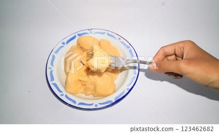 An Asian woman's hand holding a fork picks up cassava tape on a plate. Indonesia food. An Asian woman's hand holding a fork picks up cassava tape on a plate. Indonesia food. 123462682