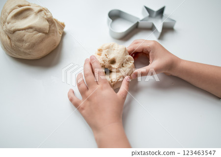 Child hands kneading dough with heart and star cookie cutters on white surface 123463547