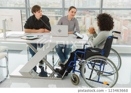 Teamwork brainstorm. Diverse multiracial colleagues woman in chair for people with disability working together. Group of people sitting in creative office discussing business. Young professional team Teamwork brainstorm. Diverse multiracial colleagues woman in chair for people with disability working together. Group of people sitting in creative office discussing business. Young professional team 123463668