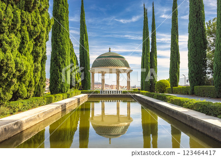 The Historical Botanical Garden La Concepcion in Malaga city at Andalusia, Spain, Europe. Serene garden gazebo reflected in a tranquil pond, surrounded by lush greenery and tall trees. 123464417