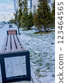 Wooden benches with a black iron base, covered with snow, stand against the background of coniferous trees and houses. Concept of recreation areas, winter. High quality photo 123464565