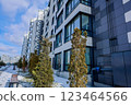 Side view of a multi-storey residential building of white gray color of modern architecture with large windows against the background of the sky with clouds, coniferous plants and a walking area with 123464566
