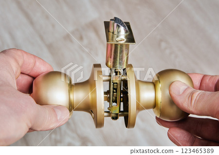Hands grip brass doorknobs exposing central shaft and lock components, demonstrating hardware internal structure for technical analysis. Hands grip brass doorknobs exposing central shaft and lock components, demonstrating hardware internal structure for technical analysis. 123465389