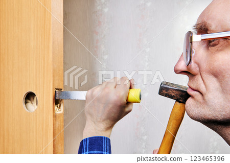 Man uses chisel to cut groove in interior door, creating recess for latch plate. Man uses chisel to cut groove in interior door, creating recess for latch plate. 123465396