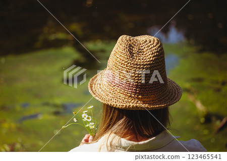 A girl wear in straw hat with a bouquet of wildflowers on a green lake shore in summer forest. Blonde woman on nature. Discover the nature world. A girl wear in straw hat with a bouquet of wildflowers on a green lake shore in summer forest. Blonde woman on nature. Discover the nature world. 123465541