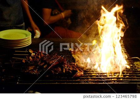 Street food hot grills with flames and smoky pork on a grill stove barbecued in a local restaurant on a night market in Thailand Street food hot grills with flames and smoky pork on a grill stove barbecued in a local restaurant on a night market in Thailand 123465798