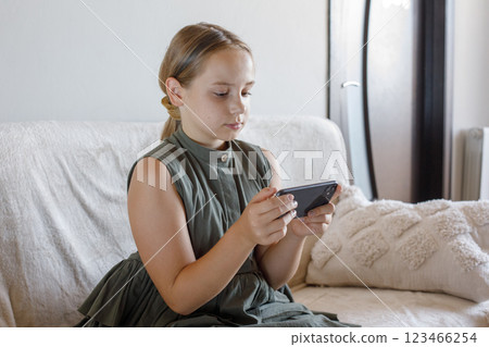 Cute young girl using the phone, playing the game, sitting on sofa at cozy home. Cute young girl using the phone, playing the game, sitting on sofa at cozy home. 123466254