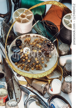 Sewing needles stuck in a green miniature spools thread Steel scissors, Spools of thread of various colour, Thimbles and Measuring tape including Pins and Buttons in small round tray. 123466412