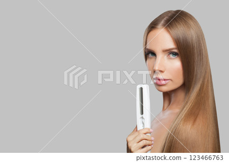 Nice brunette lady with straight hair holding straightening iron on white background. 123466763