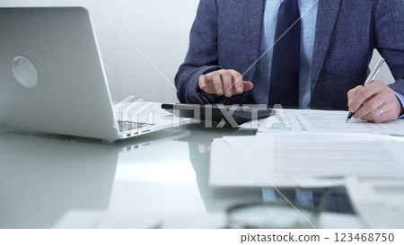 Businessman or accountant wearing blue suit is working with laptop, calculator and documents in office. Low lighting, close-up view. Business people, audit concept 123468750