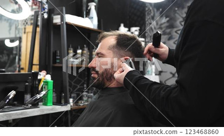 Professional barber trimming client's hair with precision, wielding scissors and comb inside contemporary grooming salon 123468860