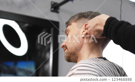 Professional barber carefully combing client's hair, preparing precise haircut in stylish barbershop, delivering contemporary men's grooming service Professional barber carefully combing client's hair, preparing precise haircut in stylish barbershop, delivering contemporary men's grooming service 123468898