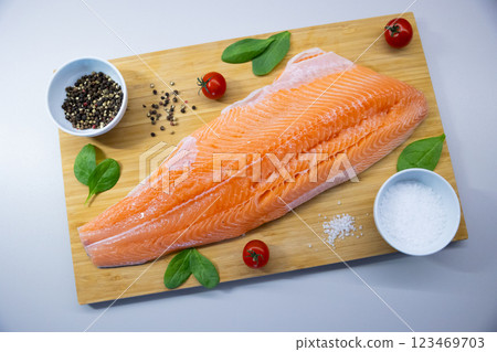 Fresh raw salmon fillet on wooden cutting board with cherry tomatoes, spinach, salt, and pepper. Healthy seafood and cooking ingredients concept. 123469703