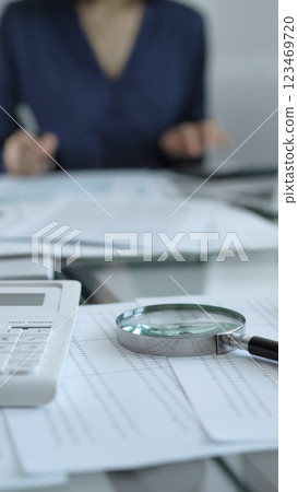 Businesswoman wearing blue dress is working with laptop, calculator and documents in a professional office setting. Low lighting, close-up vertical view. Business people, audit concept Businesswoman wearing blue dress is working with laptop, calculator and documents in a professional office setting. Low lighting, close-up vertical view. Business people, audit concept 123469720