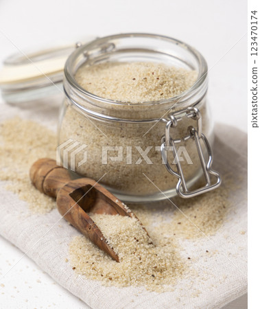 Raw uncooked fonio seeds in a wooden scoop near glass jar on white table closeup. African cereal Raw uncooked fonio seeds in a wooden scoop near glass jar on white table closeup. African cereal 123470174
