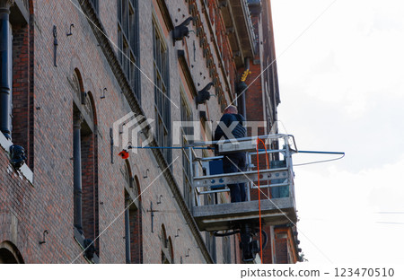 Worker cleaning the window of a building at heigt in lifting cradle. Construction workers at height working on crane in lifting bucket. Worker cleaning the window of a building at heigt in lifting cradle. Construction workers at height working on crane in lifting bucket. 123470510